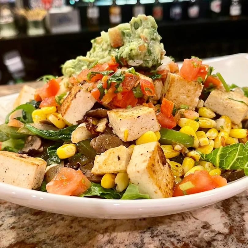 A vibrant Guac Taco & Tequila Bar salad with tofu, corn, tomatoes, and guacamole.