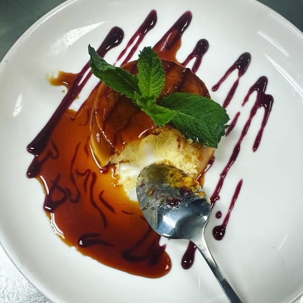 Mexican flan dessert with caramel and berry sauce, garnished with mint, on a white plate.
