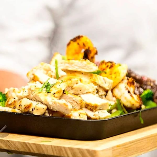 Sizzling chicken and shrimp fajitas with vegetables served in a cast iron skillet on a wooden board.
