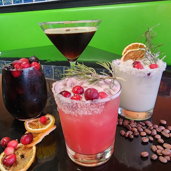 Four festive Guac Taco & Tequila Bar cocktails, garnished with cranberries, rosemary, and dried oranges.